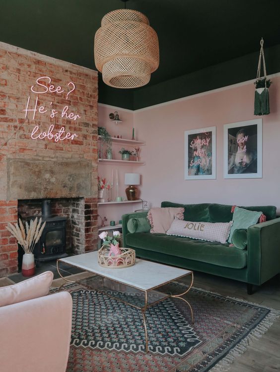 a pink and green living room with a dark green ceiling, a brick fireplace with a hearth, a green sofa and blush chair, layered rugs