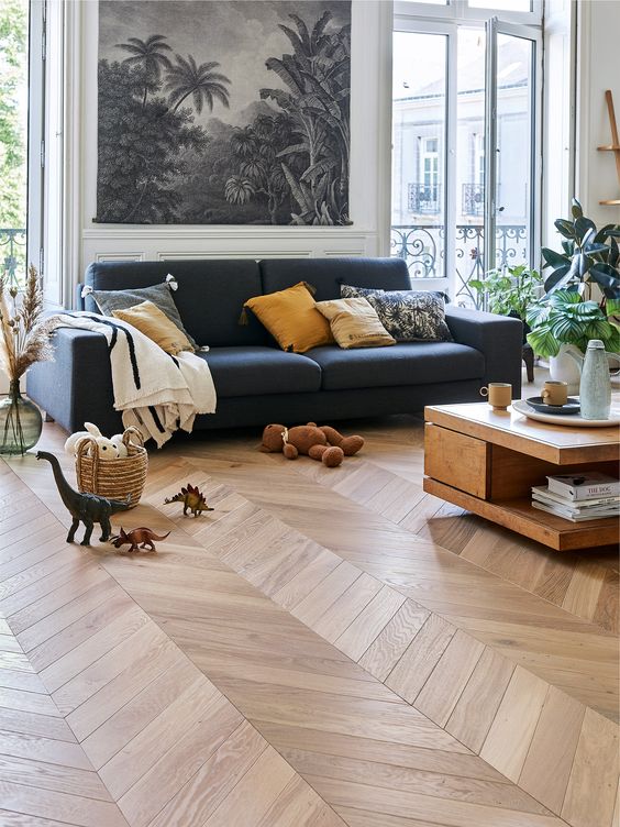 a pretty and chic living room with a lot of light, a chevron floor, a black sofa with pillows, a coffee table and lots of toys