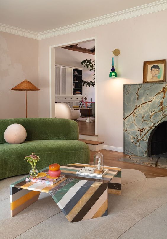 a quirky living room with a stone fireplace, a green curved sofa, a striped stone coffee table and bright and cool decor