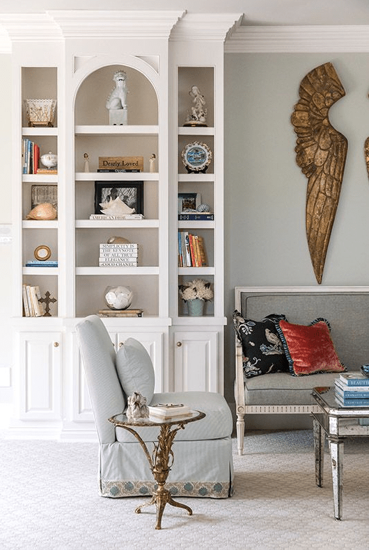 a quirky living room with a white arched bookcase, a grey refined loveseat, a light blue chair and some tables