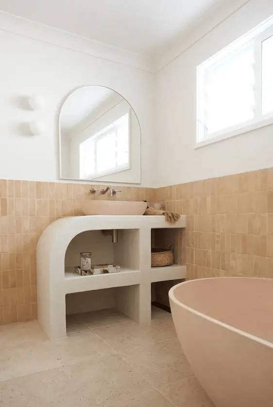 a quirky modern bathroom done with stone and terracotta tiles, a pink tub, a curved vanity and a pink sink