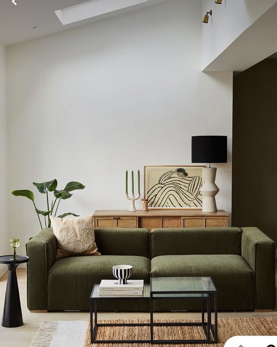 a refined contemporary living room with a low green sofa, a cane credenza, a glass coffee table, lamps and greenery