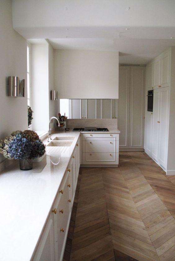 a refined creamy kitchen with a chevron floor, creamy cabinets, wall lamps and gold and brass fixtures is cool