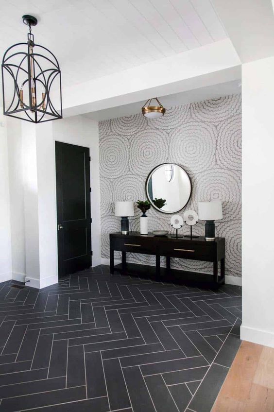 a refined entryway with a wallpaper accent wall, a black herringbone floor, a black door and a chic and refined lamp