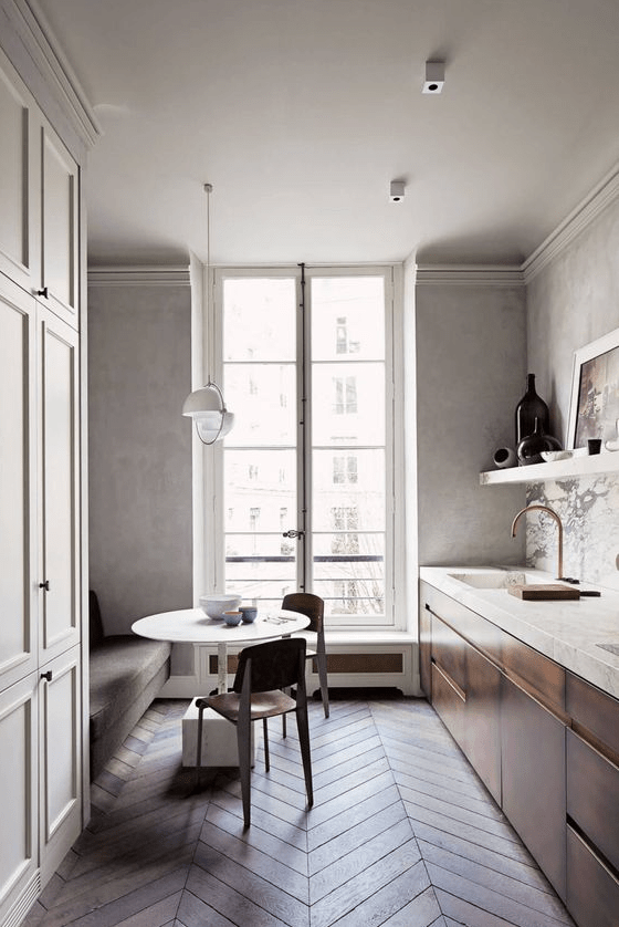 a refined kitchen with limewashed walls, a chevron floor, a grey sofa, stained cabinets and chairs is a clean and airy space