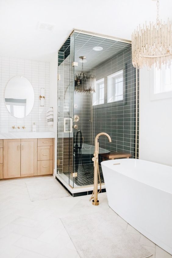 a refined modern bathroom done with stacked tiles, a shower space, a tub, a glam modern chandelier and a stained vanity plus a mirror