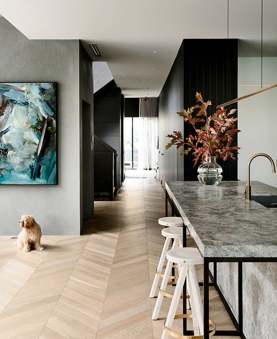 a refined modern space with grey walls and black furniture, a chevron floor, an artwork and a cool kitchen island with stools