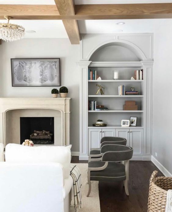 a refined neutral living room with a fireplace, an arched built-in bookcase, grey chairs and a white sofa