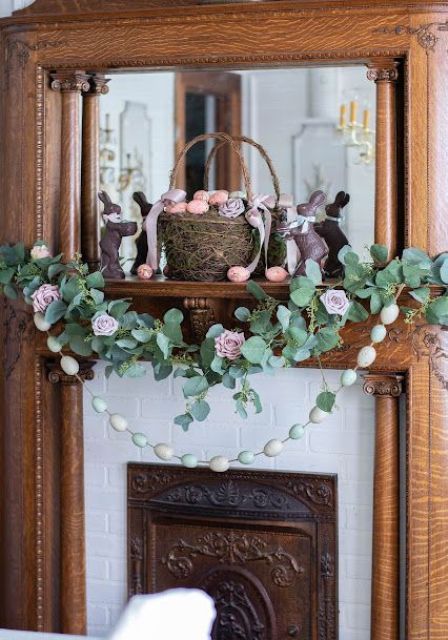 a romantic Easter mantel with greenery and faux pink roses, a pastel egg garland, a basket with eggs and fabric blooms is amazing