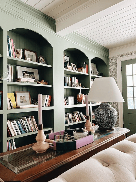 A row of arched green bookcases, a dark stained console table, a lamp and a neutral sofa and some decor