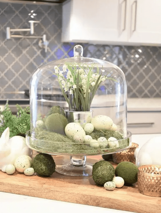 a rustic spring or Easter centerpiece of a cloche with moss, faux eggs, moss balls and a tin can with lily of the valley