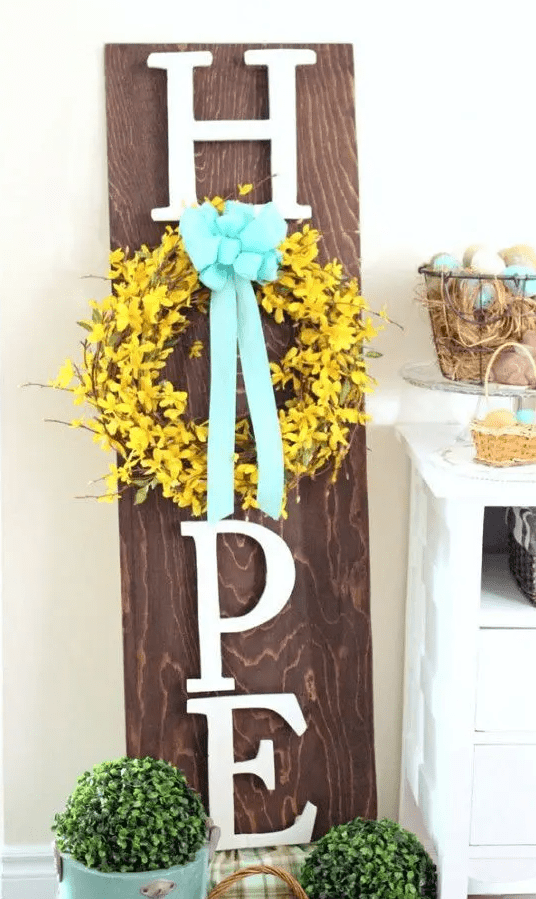 a rustic spring sign with letters, a yellow wreath and a blue bow plus potted greenery for a fresh spring feel