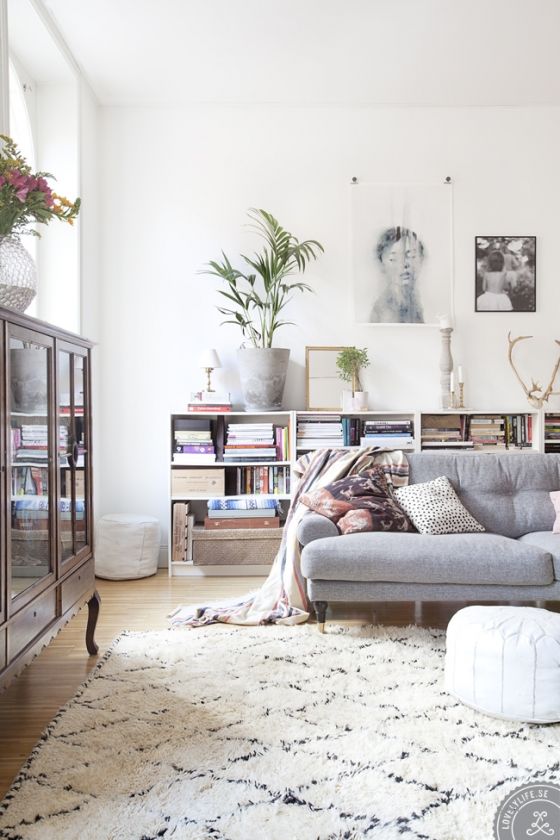 a serene Scandinavian living room with open bookshelves, a grey sofa with pillows, a vintage storage unit, some art and greenery