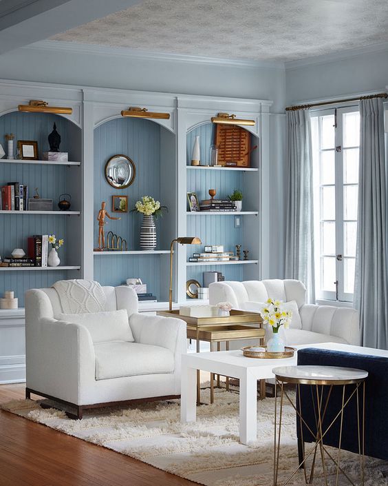 a serene coastal living room with pastel blue arched bookcases, white chairs and a navy sofa, a rug and side tables
