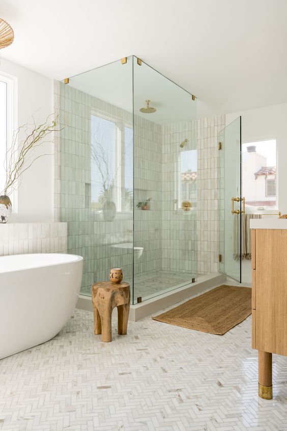 a serene contemporary bathroom done with marble and Zellige tile, a shower and a tub, a stained vanity and a wooden stool