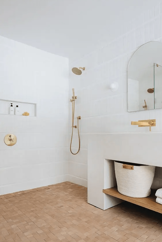 a serene white bathroom with a terracotta tile floor, a large vanity, a sink and a niche in the shower, an arched mirror