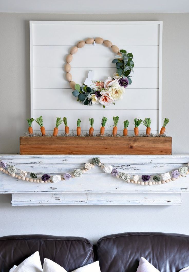 a simple rustic Easter mantel with carrots in a box, a fabric flower garland, a wooden egg and flower wreath is wow