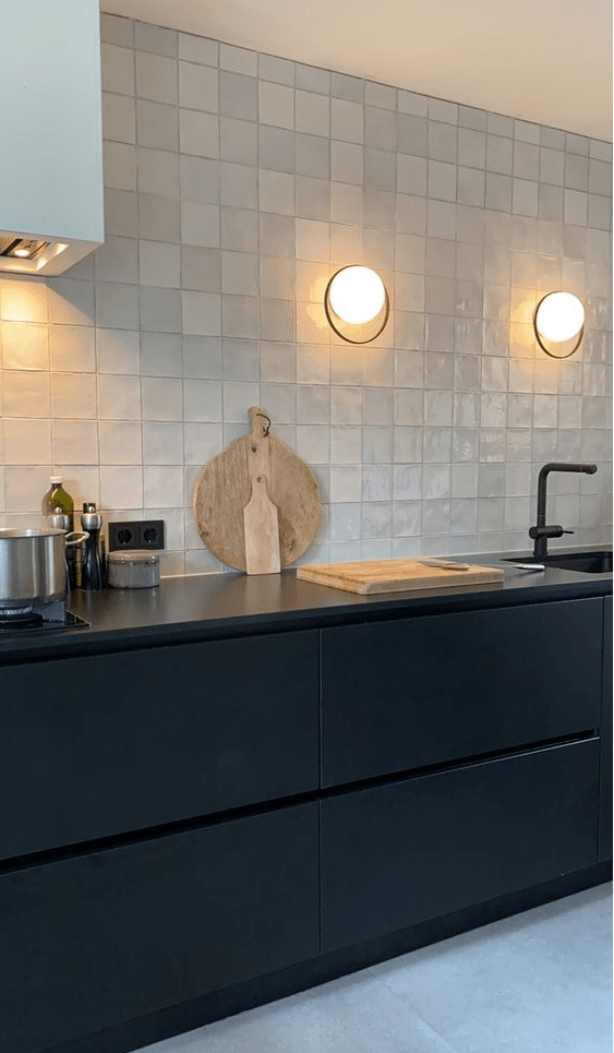 a sleek black kitchen with black countertops, black fixtures and a white Zellige tile backsplash