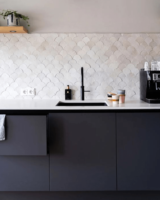 a sleek matte black kitchen with a pearly scallop tile backsplash, a white stone countertop and open shelves