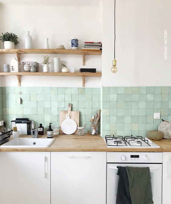 a sleek white kitchen with butcherblock countertops, a green Zellige square tile backsplash, open shelves and pendant lamps