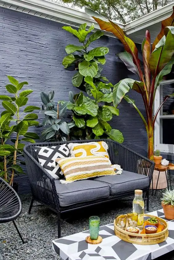 a small and bright patio with black rattan furniture and colorful pillows, a printed table and potted statement plants