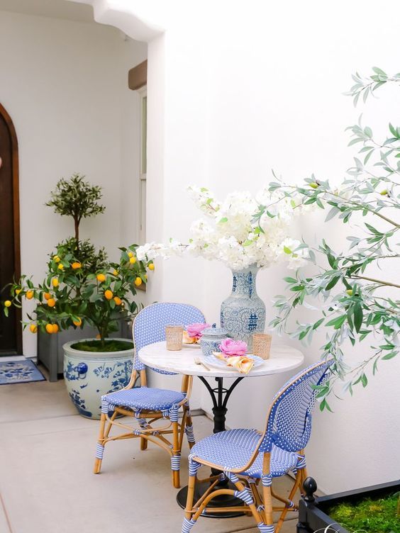 a small and bright patio with blue rattan chairs, a small table and beautiful potted plants is wow