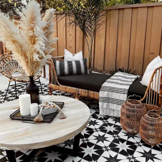 a small and cool black and white farmhouse patio clad with star tile, rattan furniture, a coffee table with lovely decor, lanterns and textiles