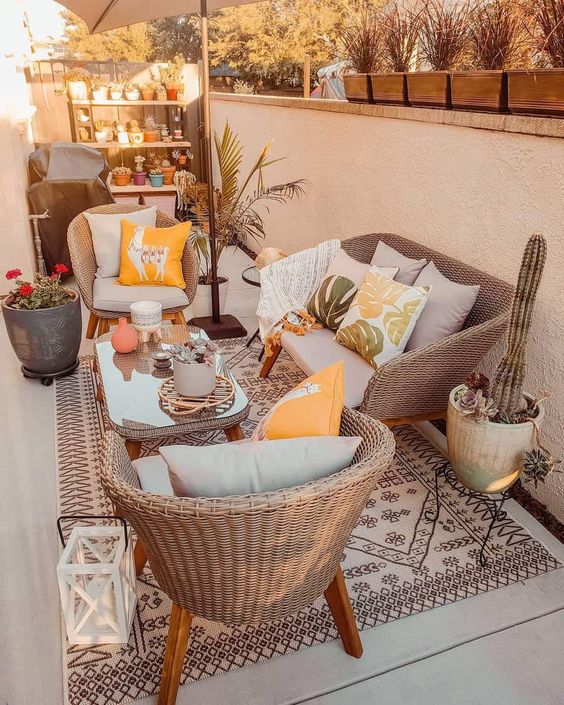 a small and cool patio with wicker furniture, a coffee table, potted plants, a shelf with potted plants and an umbrella