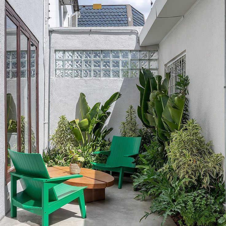 a small and fresh patio with lots of greenery, a low coffee table and a couple of green wooden chairs is amazing