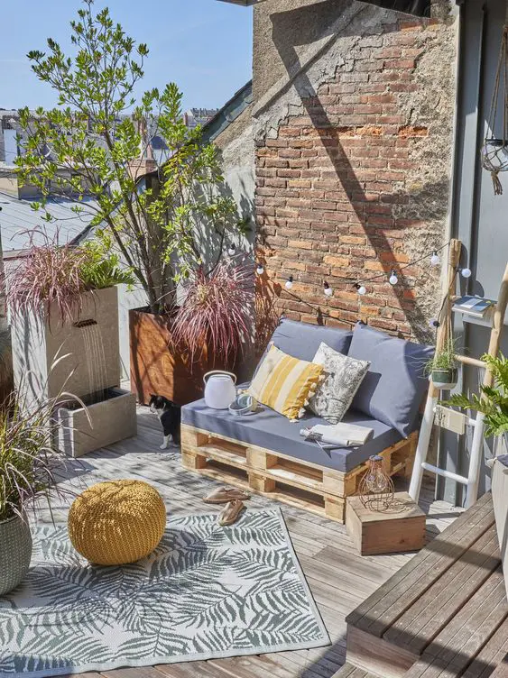 a small patio with a pallet sofa and pillows, potted plants, string lights and a printed rug