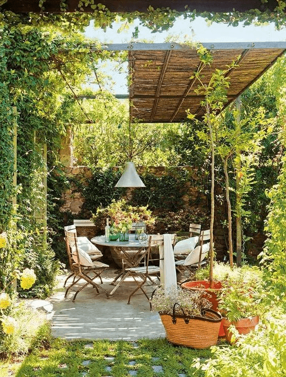 a small patio with a roof, a dining set with folding chairs, greenery and blooms that slowly flows into a garden
