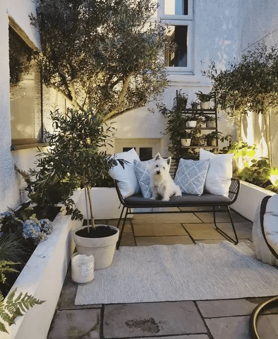 a small patio with a stone deck, a modern bench, potted plants and blooms and lights along the patio