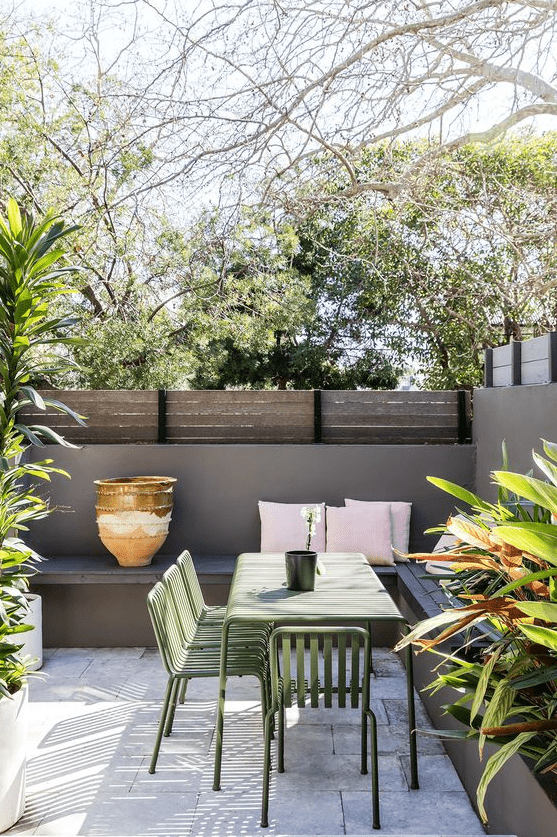 a small patio with a tile floor, a corner built-in bench, lots of potted greenery around and a dining set