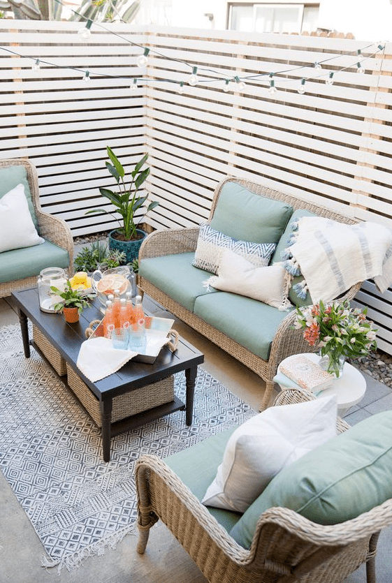 a small patio with wicker furniture, a black coffee table, some potted greenery and blooms and string lights over the space