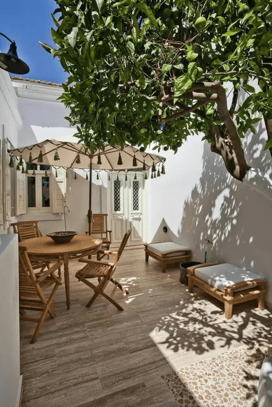 a small yet cool patio done Mediterranean style with a deck, a wooden dining set, a couple of seats and a living tree