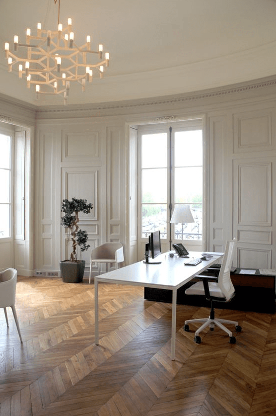 a sophisticated home office with molding, chevron floor, a white desk and some chairs, greenery and a cool chandelier
