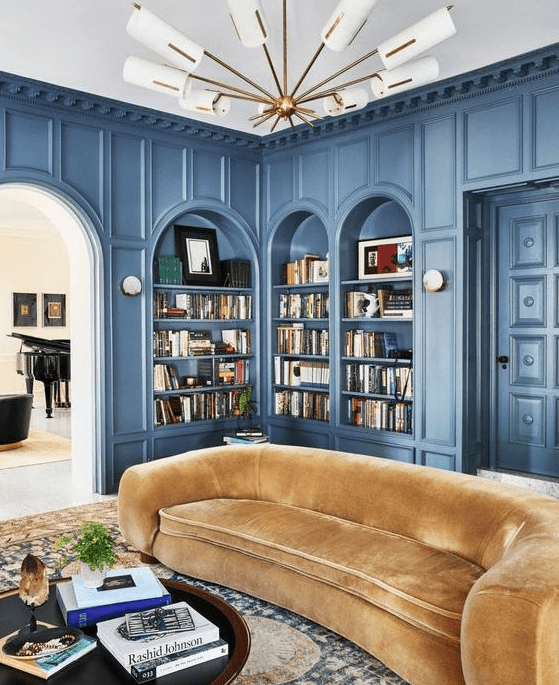 a sophisticated living room with blue arched bookcases and shelves, a yellow curved sofa, a printed rug and a coffee table with decor