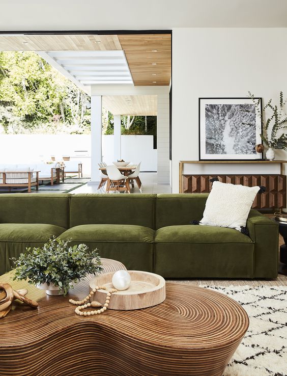 a sophisticated space with a low green velvet sofa, a unique curved coffee table, a console with decor and entrace to the terrace