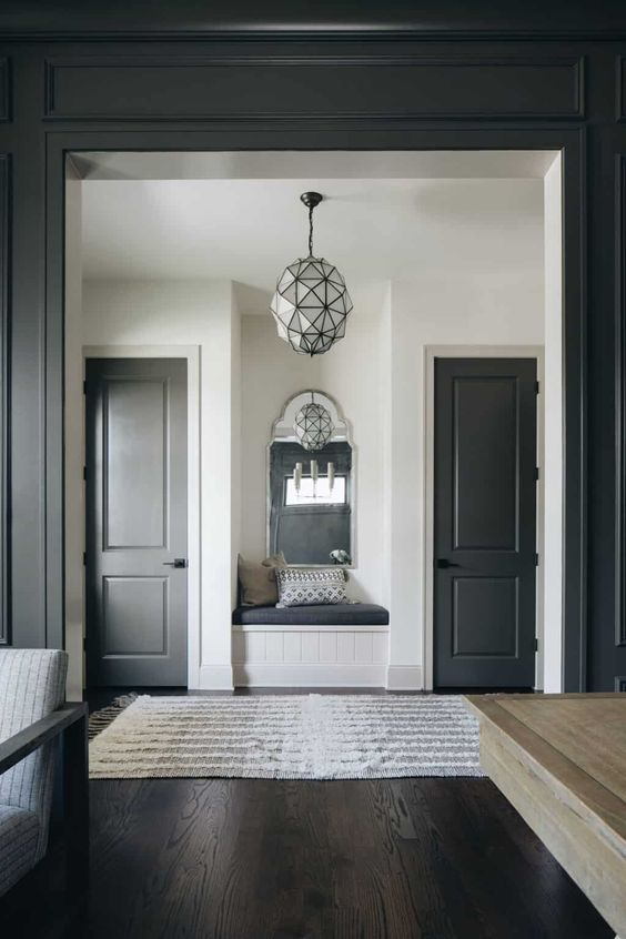 a stylish farmhouse space with white walls, soot doors and doorway, a built-in seat and a lovely faceted pendant lamp