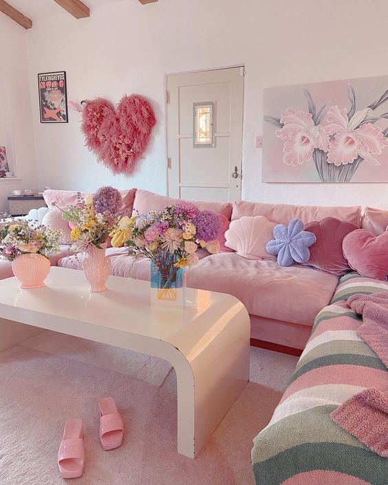 a super cute and fun dopamine decor living room with a pink sectional, colorful and pastel pillows, a curved table with blooms and a pink heart