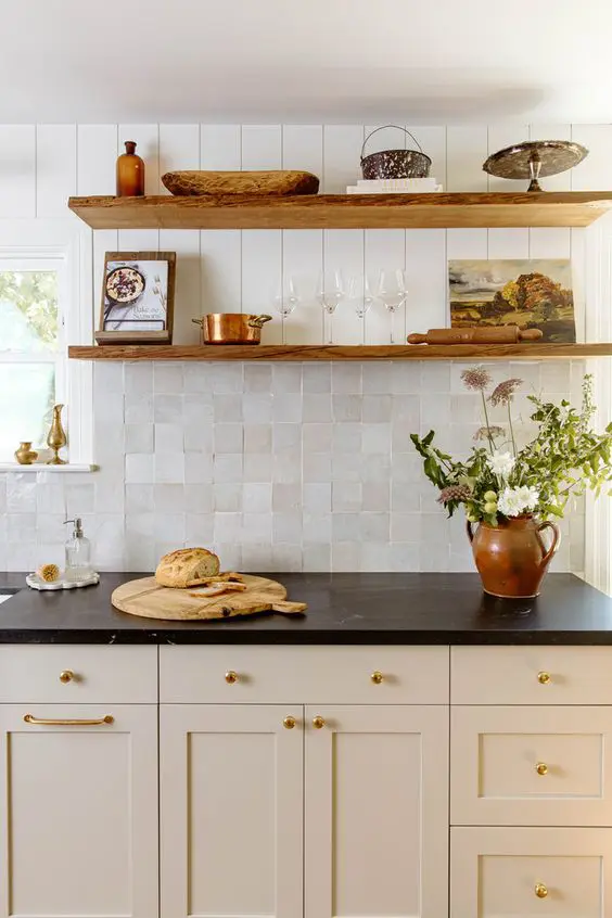 a tan farmhouse kitchen with black countertops, a neutral Zellige tile and planked backsplash and open shelves