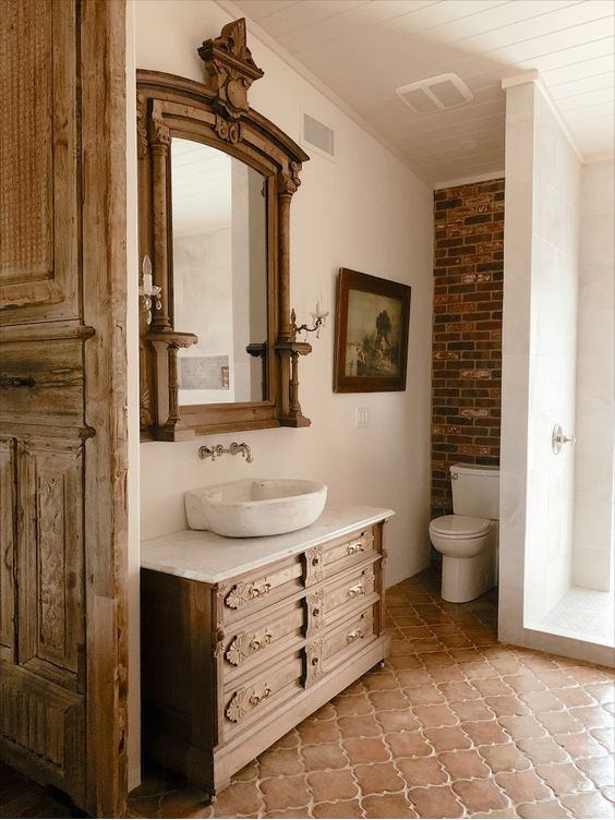a vintage bathroom clad with Moroccan terracotta tiles, a stained vanity, a mirror in a stained frame and a red brick accent