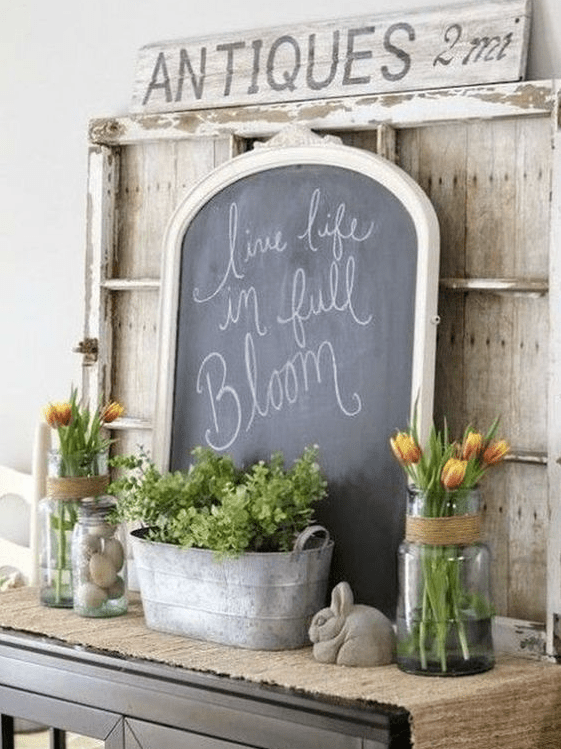 a vintage farmhouse mantel with tulips in clear vases, potted greenery, a chalkboard sign, fake eggs and a rabbit