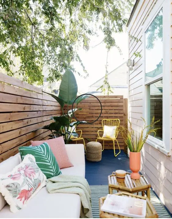 a vivacious patio with rugs, a daybed with pillows, yellow chairs, potted plants, bamboo coffee tables