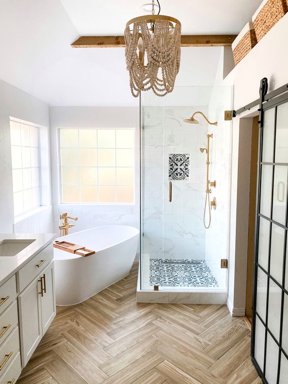 a welcoming bathroom with windows, a shower space, a tub, a wooden bead chandelier, a vanity and brass fixtures