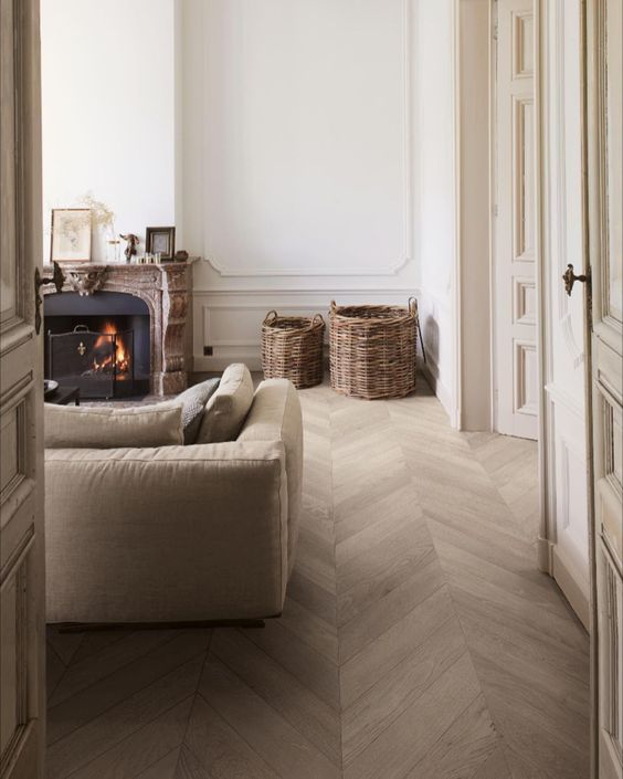 a welcoming neutral living room with molding, a chevron floor, a tan sofa, a fireplace clad with stone and baskets