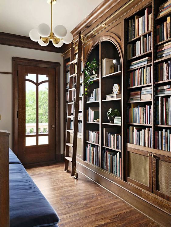 a welcoming space with a stained arched bookcase and shelves, a navy sofa and a ladder is ideal to enjoy reading
