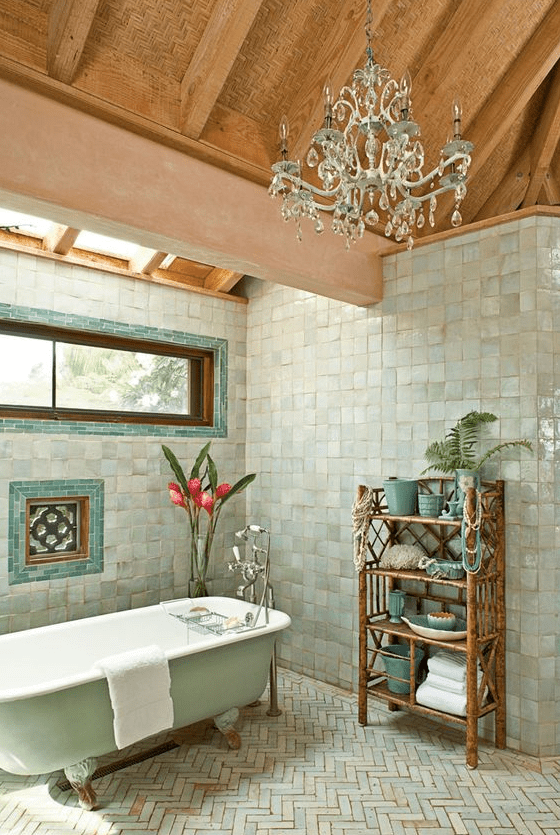 a whimsical bathroom clad with Zellige square and herringbone tiles, a mint tub, a skylight and window, a chic chandelier