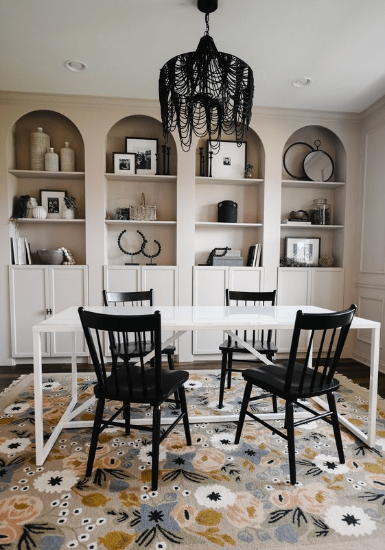 a whimsical home office with tan arched bookcases with black and white decor, a white desk, black chairs and a black chandelier