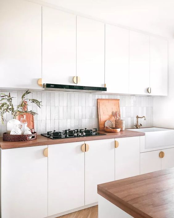 a white Scandinavian kitchen with stained butcherblock countertops, a white Zellige tile backsplash and cool gold knobs